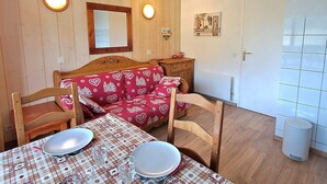 A cozy room with a wooden bed, a dining table set for two, and a white door. - Calm T2 apartment, slopes access, private parking (Les Deux Alpes)