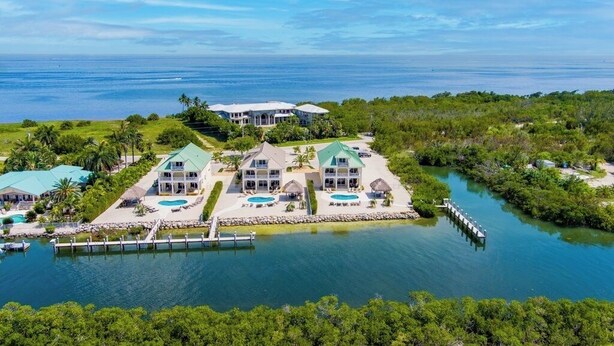 Een groot, meerhoog resort met meerdere zwembaden, een steiger en weelderige begroeiing.
