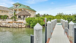 Hotel aan het water met een rieten dak, een bestraat steiger en weelderige begroeiing.