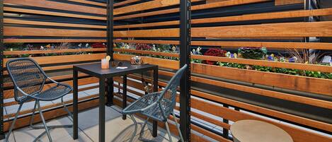 A seating area with two chairs and a table, surrounded by wooden slats and a planter with flowers.