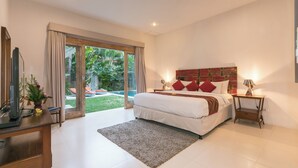 A modern bedroom with a large bed, a TV, a desk, and a view of a garden through a sliding door.