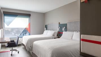 A hotel room with two beds, a desk, and a chair. There is a window with a view of the city.