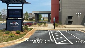 A parking area with EV charging stations, a building with a red facade, and a clear sky. - avid hotels Perry-National Fairground Area by IHG (Perry)