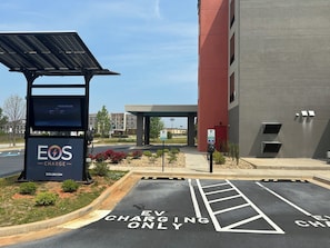 A parking area with EV charging stations, a building with a red facade, and a clear sky. - avid hotel Perry-National Fairground Area by IHG (Perry)