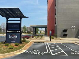 Un área de estacionamiento con estaciones de carga para vehículos eléctricos, un edificio de fachada roja y cielo despejado.