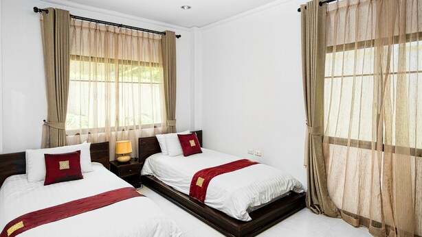 Quarto de hotel com duas camas, cortinas bege, roupa de cama branca e cabeceira de madeira.