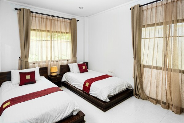 A hotel room with two beds, beige curtains, white bedding, and a wooden headboard.