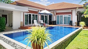 Piscina com deck azulejado, cercada por gramado e plantas em vasos.