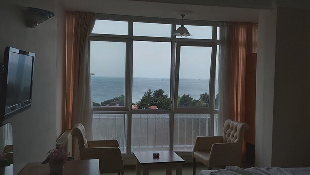 A hotel room with a large window offering a view of the sea. There is a bed, a table, and two chairs. - Sancak Hotel (Istanbul)