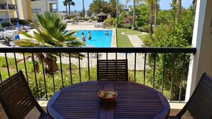 A balcony with a view of a swimming pool, palm trees, and a building in the background. - Clube Alvor Ria 103 Luxury sea view 1bed apartment outstanding central location. (Alvor)