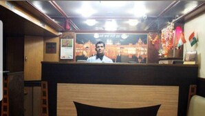 A room with a wooden headboard, a bed, a desk with a chair, and a wall with a calendar and a flag. - Hotel Diamond (Mumbai)