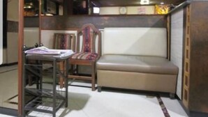 A compact room with a sofa, a wooden chair, and a small table with papers. - Hotel Diamond (Mumbai)