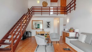A spacious living area with a wooden staircase, a dining table with chairs, a sofa, and a kitchen area with a microwave and a basket. - "Casas Azalea - Oceanfront Home with Sunset Views" (Mosteiros)