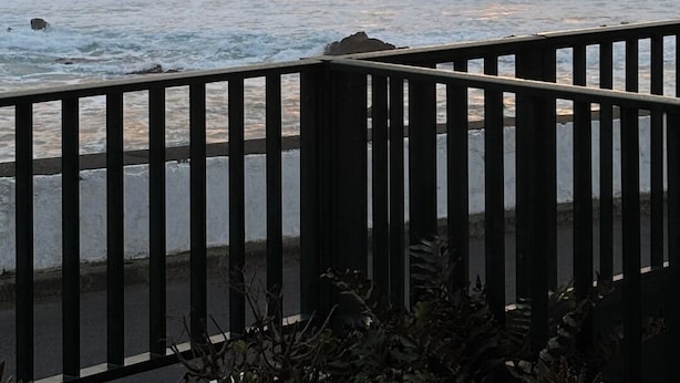A coastal sunset with a large rock formation, waves, and a wooden railing. - "Casas Azalea - Oceanfront Home with Sunset Views" (Mosteiros)