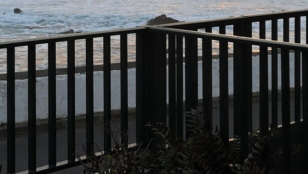 A coastal sunset with a large rock formation, waves, and a wooden railing. - Casas Hortênsia - Oceanfront Home w/ Sunset Views (Mosteiros)
