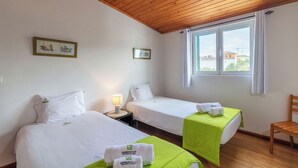 A hotel room with two beds, a wooden ceiling, a window with a view, and a chair. - Casas Hortênsia - Oceanfront Home w/ Sunset Views (Mosteiros)
