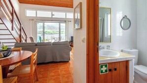 A modern interior with a dining area, a sofa, a staircase, and a bathroom with a large mirror and a toilet. - Casas Hortênsia - Oceanfront Home w/ Sunset Views (Mosteiros)