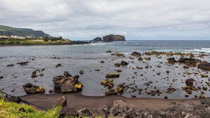A rocky beach with scattered boulders and a distant view of a mountainous coastline. - Casas Hortênsia - Oceanfront Home w/ Sunset Views (Mosteiros)