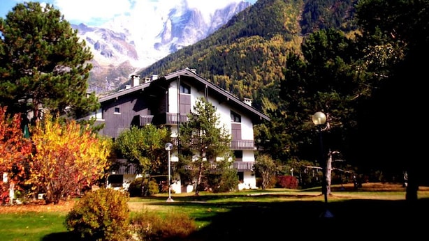 A chalet-style building with a sloped roof, surrounded by a well-maintained garden with various shrubs and trees.