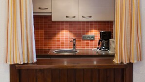 A small kitchenette with a sink, a coffee maker, and a tiled backsplash.