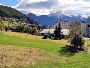 Ein Hotel mit flachem Dach und mehreren Etagen, umgeben von einer Wiese und Bäumen, mit Bergen im Hintergrund.