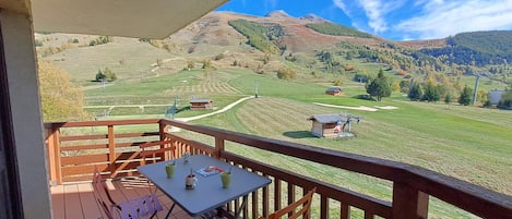 A balcony with a table and chairs, overlooking a green landscape with hills and a clear sky.