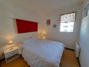A bedroom with a bed, bedside lamps, a red curtain, a star decoration, and a window with a view.