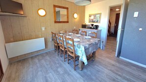 Un coin repas avec une table en bois dressée pour quatre personnes, entourée de chaises, d’un luminaire suspendu et d’un miroir au mur.