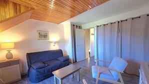 Une pièce chaleureuse avec un plafond en bois, un canapé, un fauteuil, une petite table et une lampe.