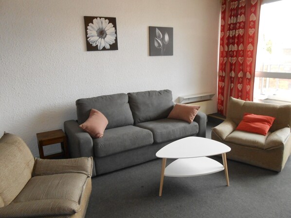 En stue med en grå sofa, to lænestole, et lille bord og to billeder på væggen.