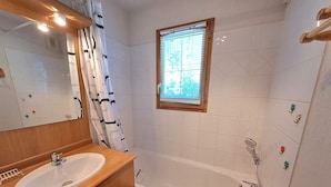 A bathroom with a wooden vanity, a bathtub, a window with blinds, and a mirror. - Charming 2-bedroom apartment for 5 people in Les Deux Alpes (Les Deux Alpes)