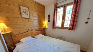 A wooden-paneled room with a bed, two bedside lamps, a window with curtains, and a wall-mounted picture. - Charming 2-bedroom apartment for 5 people in Les Deux Alpes (Les Deux Alpes)