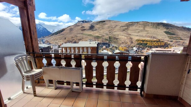 A balcony with a view of a mountainous landscape, a chair, and a small table.
