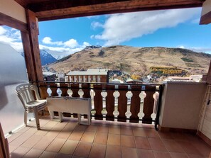 A balcony with a view of a mountainous landscape, a chair, and a small table.