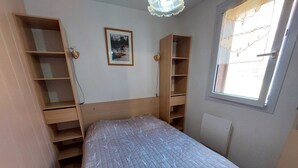 A bedroom with a bed, wooden shelving units, a framed picture on the wall, and a window with a view.