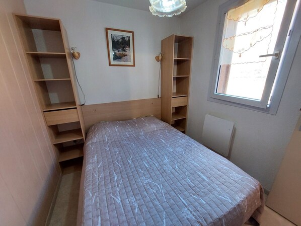 A bedroom with a bed, wooden shelving units, a framed picture on the wall, and a window with a view.