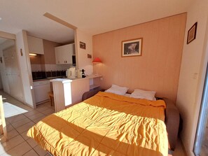 Une chambre d’hôtel compacte comprenant un lit, une kitchenette et un petit coin repas.