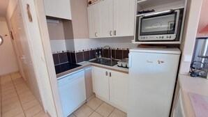 A compact kitchen with white cabinets, a black countertop, a built-in microwave, and a refrigerator.