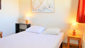 A hotel room with a bed, two bedside tables with lamps, a wall-mounted painting of polar bears, and a red curtain.