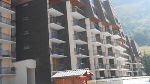A multi-story residential building with balconies, a small wooden structure, and a mountainous backdrop.