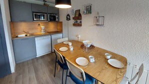 Une cuisine compacte dotée d’appareils électroménagers modernes, une table à manger avec des chaises et un luminaire suspendu.