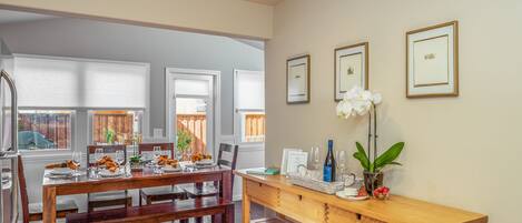 A dining area with a wooden table set for four, a bench, and a side table with a vase of flowers and a bottle.