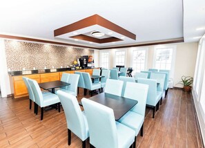 Un comedor moderno con sillas azul claro y mesas oscuras, una cocina con salpicadero de mosaicos e iluminación empotrada en el techo.