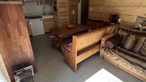 A rustic cabin interior with a wooden dining table, a sofa, and a kitchen area with wooden cabinets and a stone fireplace.