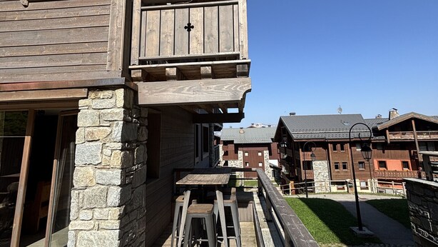 A wooden building with balconies, stone pillars, and outdoor seating.