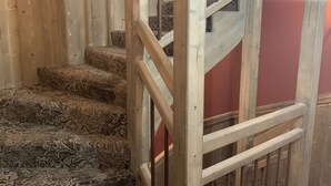 A staircase with patterned carpet, wooden railings, and a red wall.