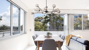 A modern dining area with a glass table, grey chairs, and a chandelier. - Perfect Located 2-Bed with Spacious Balcony & BBQ (Cremorne)