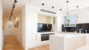 A modern kitchen with white cabinetry, a central island, and pendant lighting. - Perfect Located 2-Bed with Spacious Balcony & BBQ (Cremorne)