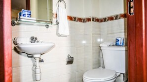 A bathroom with a white sink, toilet, and a shelf with toiletries. - Affordable furnished studio apartment (Nairobi)