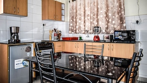 A compact kitchen with wooden cabinets, a refrigerator, a microwave, and a dining table with chairs. - Affordable furnished studio apartment (Nairobi)